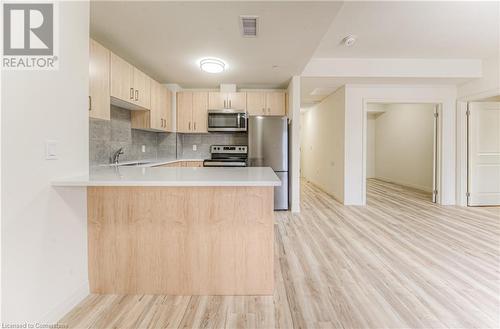 Kitchen featuring kitchen peninsula, appliances with stainless steel finishes, light wood-type flooring, tasteful backsplash, and light brown cabinetry - 301 Westmount Road W Unit# 414, Kitchener, ON - Indoor Photo Showing Kitchen