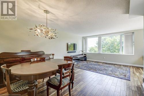 Dining area featuring hardwood / wood-style floors, a textured ceiling, and an inviting chandelier - 77 Governors Road Unit# 501, Dundas, ON - Indoor Photo Showing Dining Room