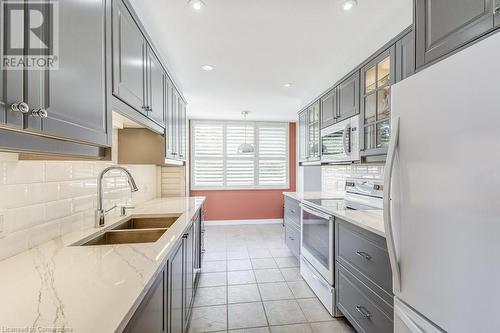 Kitchen with gray cabinetry, white appliances, sink, decorative backsplash, and light stone counters - 77 Governors Road Unit# 501, Dundas, ON - Indoor Photo Showing Kitchen With Double Sink