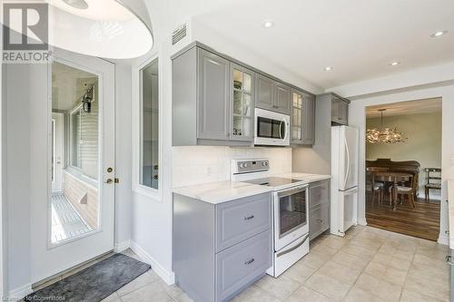 Kitchen featuring gray cabinetry, light stone counters, decorative light fixtures, white appliances, and light tile patterned floors - 77 Governors Road Unit# 501, Dundas, ON - Indoor Photo Showing Kitchen