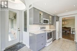 Kitchen featuring gray cabinetry, light stone counters, decorative light fixtures, white appliances, and light tile patterned floors - 