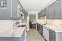 Kitchen with gray cabinets, white appliances, sink, and light tile patterned floors - 