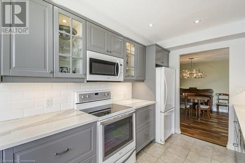 Kitchen featuring white appliances, decorative light fixtures, light hardwood / wood-style flooring, gray cabinets, and a notable chandelier - 77 Governors Road Unit# 501, Dundas, ON - Indoor Photo Showing Kitchen