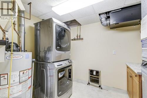 Washroom with cabinets, stacked washer / dryer, and water heater - 77 Governors Road Unit# 501, Dundas, ON - Indoor Photo Showing Laundry Room