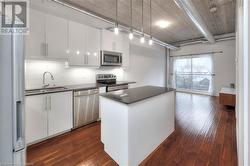 Kitchen with white cabinetry, sink, dark wood-type flooring, hanging light fixtures, and appliances with stainless steel finishes - 