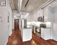 Kitchen featuring white cabinets, hanging light fixtures, appliances with stainless steel finishes, and dark wood-type flooring - 