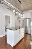 Kitchen with white cabinets, pendant lighting, dark hardwood / wood-style flooring, and stainless steel refrigerator - 