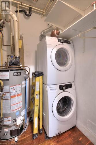 Clothes washing area featuring dark hardwood / wood-style flooring, gas water heater, and stacked washing maching and dryer - 15 Devitt Avenue S Unit# 103, Waterloo, ON - Indoor Photo Showing Laundry Room