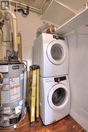 Clothes washing area featuring dark hardwood / wood-style flooring, gas water heater, and stacked washing maching and dryer - 