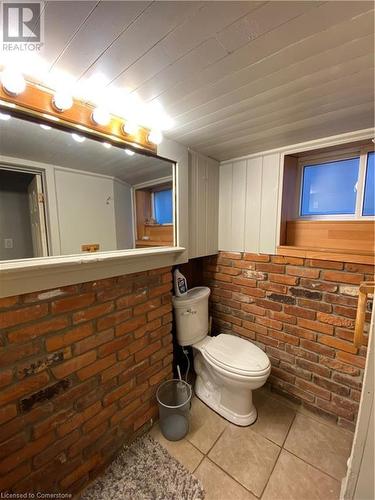 Bathroom featuring tile patterned flooring, toilet, and brick wall - 522 Roxborough Avenue Unit# #1, Hamilton, ON - Indoor Photo Showing Bathroom