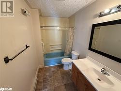 Full bathroom with a baseboard heating unit, a textured ceiling, toilet, shower / bath combo with shower curtain, and vanity - 