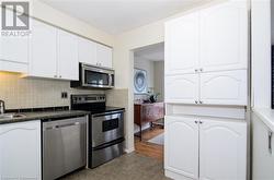 Kitchen with light wood-type flooring, stainless steel appliances, white cabinetry, and sink - 