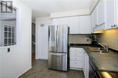 Kitchen with sink, dark tile patterned floors, decorative backsplash, white cabinets, and appliances with stainless steel finishes - 79 Braeheid Avenue Avenue Unit# 6, Hamilton, ON - Indoor Photo Showing Kitchen With Stainless Steel Kitchen With Double Sink