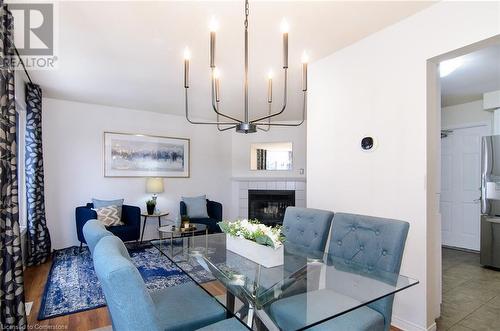 Dining area featuring a tiled fireplace, a notable chandelier, and hardwood / wood-style flooring - 79 Braeheid Avenue Avenue Unit# 6, Hamilton, ON - Indoor Photo Showing Dining Room With Fireplace