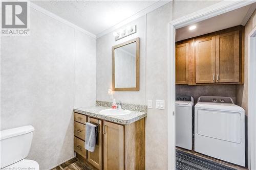 Bathroom featuring separate washer and dryer, wood-type flooring, a textured ceiling, toilet, and ornamental molding - 99 Fourth Conc Road, Burford, ON - Indoor Photo Showing Laundry Room