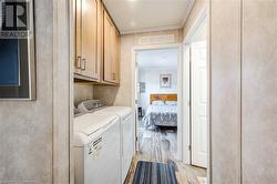 Clothes washing area with cabinets, light hardwood / wood-style flooring, washer and dryer, and ornamental molding - 