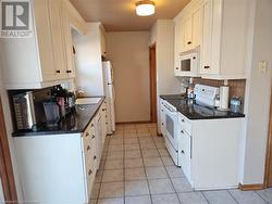 Kitchen featuring tasteful backsplash, white cabinets, light tile patterned flooring, and white appliances - 