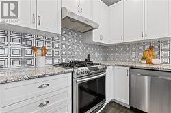 Kitchen with white cabinetry, light stone countertops, dark hardwood / wood-style floors, decorative backsplash, and appliances with stainless steel finishes - 