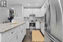 Kitchen featuring decorative backsplash, appliances with stainless steel finishes, light stone counters, white cabinets, and dark hardwood / wood-style floors - 