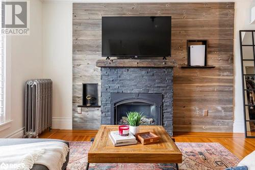 Family room featuring radiator, wood walls, fireplace, and hardwood flooring - 109 Fairleigh Avenue S, Hamilton, ON - Indoor Photo Showing Living Room With Fireplace