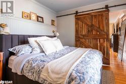 Bedroom featuring ornamental molding, hardwood floors, and a barn door - 