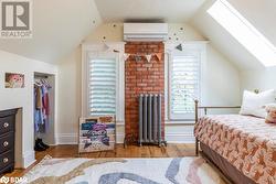 Bedroom with lofted ceiling with skylight, radiator, wood flooring, and an AC wall unit - 