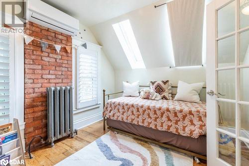 Bedroom featuring vaulted ceiling with skylight, radiator, light wood flooring, and a wall mounted air conditioner - 109 Fairleigh Avenue S, Hamilton, ON - Indoor Photo Showing Bedroom