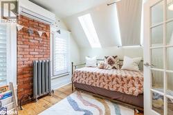 Bedroom featuring vaulted ceiling with skylight, radiator, light wood flooring, and a wall mounted air conditioner - 