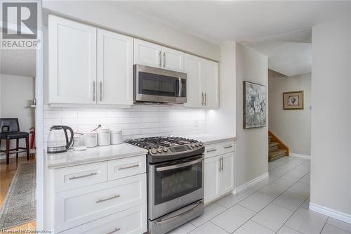 Kitchen featuring white cabinetry, backsplash, a textured ceiling, light tile patterned floors, and appliances with stainless steel finishes - 134 Bayne Crescent, Cambridge, ON 