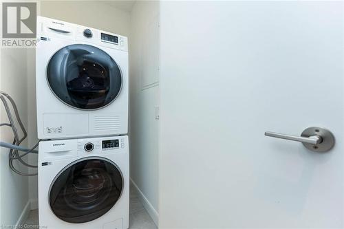 Clothes washing area featuring stacked washing maching and dryer and light tile patterned floors - 741 King Street W Unit# 301, Kitchener, ON - Indoor Photo Showing Laundry Room