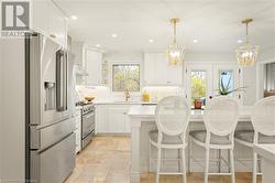 Kitchen with a wealth of natural light, white cabinetry, stainless steel appliances, and decorative light fixtures - 