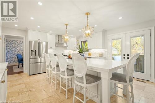 Kitchen with pendant lighting, white cabinetry, wall chimney range hood, and stainless steel refrigerator with ice dispenser - 659 Deervalley Road, Ancaster, ON - Indoor