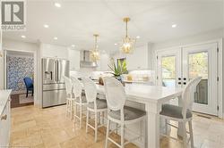 Kitchen with pendant lighting, white cabinetry, wall chimney range hood, and stainless steel refrigerator with ice dispenser - 