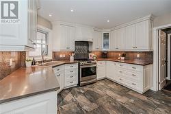 Kitchen featuring custom exhaust hood, white cabinets, sink, stainless steel gas range, and kitchen peninsula - 