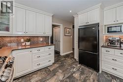 Kitchen featuring black refrigerator, stove, backsplash, and white cabinetry - 