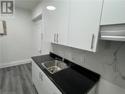 Kitchen with decorative backsplash, sink, white cabinets, and wood-type flooring - 660 Main Street E Unit# 1, Hamilton, ON - Indoor Photo Showing Kitchen With Double Sink