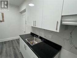 Kitchen with decorative backsplash, sink, white cabinets, and wood-type flooring - 