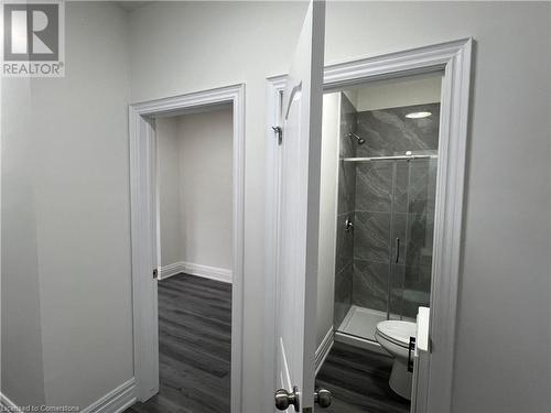 Bathroom featuring wood-type flooring, toilet, and a shower with shower door - 660 Main Street E Unit# 1, Hamilton, ON - Indoor Photo Showing Bathroom