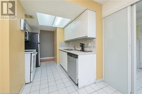 Kitchen with backsplash, stainless steel appliances, sink, light tile patterned floors, and white cabinets - 305 Webb Drive Unit# 308, Mississauga, ON 