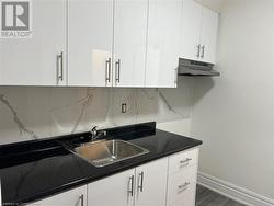 Kitchen featuring backsplash, white cabinetry, sink, and dark wood-type flooring - 