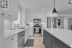 Kitchen featuring sink, white cabinets, decorative light fixtures, and appliances with stainless steel finishes - 