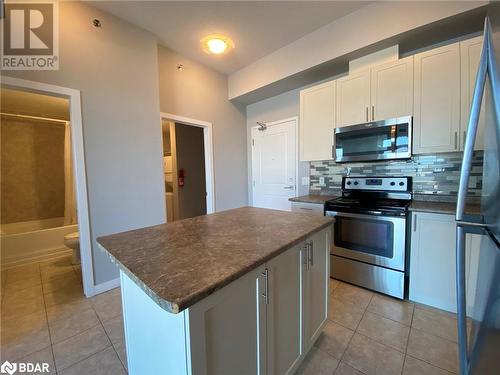 Kitchen with backsplash, light tile patterned floors, appliances with stainless steel finishes, a kitchen island, and white cabinetry - 2486 Old Bronte Road Unit# 813, Oakville, ON 