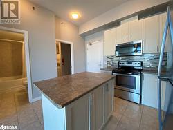 Kitchen with backsplash, light tile patterned floors, appliances with stainless steel finishes, a kitchen island, and white cabinetry - 