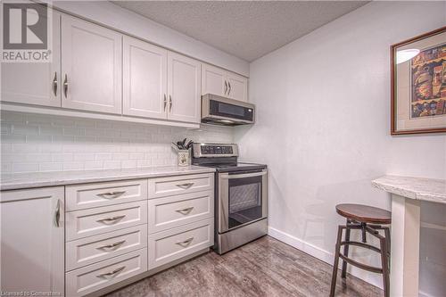 Kitchen with backsplash, a textured ceiling, light hardwood / wood-style floors, white cabinetry, and stainless steel appliances - 55 Green Valley Drive Drive Unit# 1806, Kitchener, ON - Indoor Photo Showing Kitchen