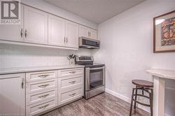 Kitchen with backsplash, a textured ceiling, light hardwood / wood-style floors, white cabinetry, and stainless steel appliances - 