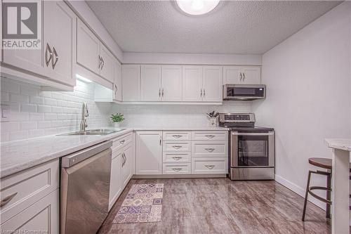 Kitchen featuring white cabinets, sink, a textured ceiling, appliances with stainless steel finishes, and light hardwood / wood-style floors - 55 Green Valley Drive Drive Unit# 1806, Kitchener, ON - Indoor Photo Showing Kitchen With Double Sink