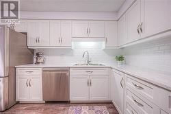 Kitchen with light stone countertops, tasteful backsplash, stainless steel appliances, sink, and white cabinetry - 