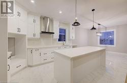 Kitchen with a center island, sink, wall chimney exhaust hood, decorative light fixtures, and white cabinets - 