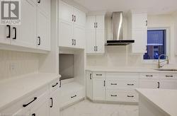 Kitchen with decorative backsplash, white cabinetry, wall chimney exhaust hood, and sink - 