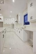 Kitchen featuring backsplash, sink, white cabinets, and wall chimney range hood - 